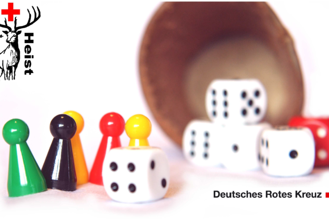 Das Bild zeigt einen Würfelbecher mit Würfeln und bunten Spielfiguren.